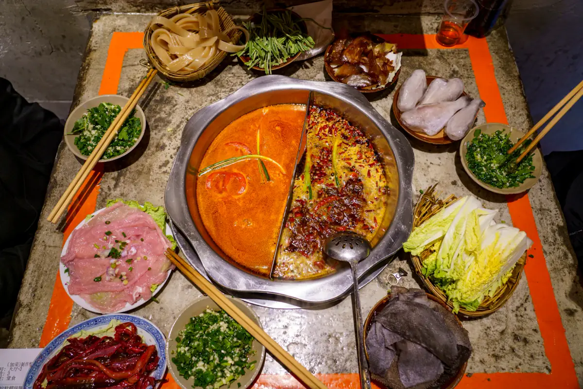 A bubbling red Chongqing hot pot surrounded by shared dishes at a table